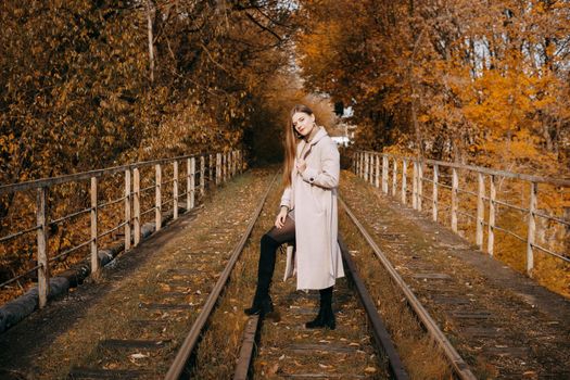 A beautiful long-haired woman walks through the autumn streets. Railway, autumn leaves, a woman in a light coat.