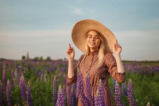 A beautiful woman in a straw hat walks in a field with purple flowers. A walk in nature in the lupin field.