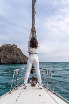 Woman standing on the nose of the yacht at a sunny summer day, breeze developing hair, beautiful sea on background.