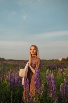 A beautiful woman in a straw hat walks in a field with purple flowers. A walk in nature in the lupin field.