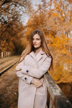 A beautiful long-haired woman walks through the autumn streets. Railway, autumn leaves, a woman in a light coat.