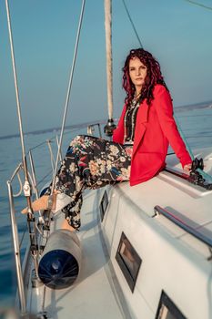 A woman sits on the bow of a yacht on a sunny summer day, the breeze develops her hair, a beautiful sea is in the background.