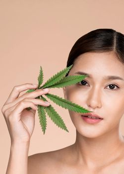 Closeup portrait of young ardent girl with healthy fresh skin holding green hemp leaf. Combination of beauty and cannabis concept.