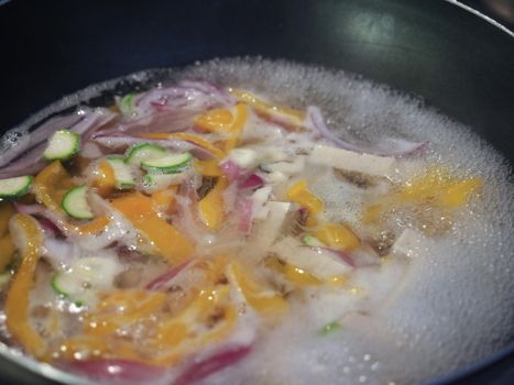 preparation of asian food with chopped vegetables and tofu frying in a pan