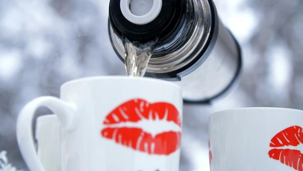 on a background of a winter forest, close-up, froon a background of a winter forest, close-up, from a thermos poured tea into cups. on the cups, sponges are drawnm a thermos poured tea into cups. on the cups, sponges are drawn. High quality photo