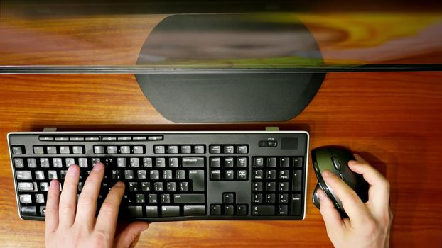 timlamps, close-up, view from the top, men's hands typing on computer keyboard with a computer mouse, in front of the monitor. Businessman working, Blogger, journalist writing. High quality photo
