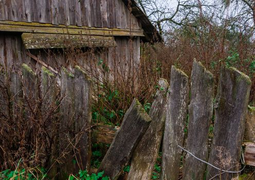 Old fallen down bent fence in the background of the yard. Old abandoned yard with broken fence and high grass. Autumn village landscape.