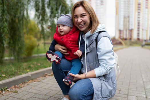 portrait of a young mother woman with her one-year-old child in her arms against the backdrop of a city park.