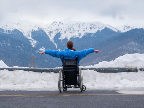 Rear view of a woman in a wheelchair spread her arms to the side like wings in the mountains in winter