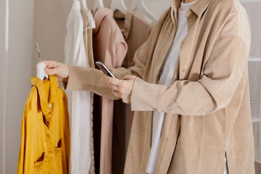 Woman holding smartphone and taking photo of her old clothes to sell them online. Selling on website, e-commerce. Reuse, second-hand concept. Conscious consumer, sustainable lifestyle. Close-up view