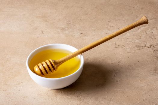 A bowl of honey and a wooden spoon for honey on a light surface. Selective focus.