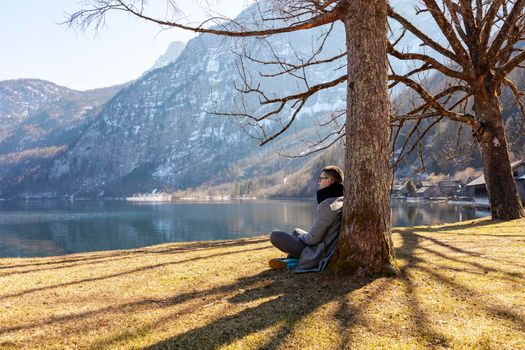 Young man sitting outdoors and enjoying mountains, snow, lake, good weather, blue sky, sun. Beautiful landscape. Time with yourself, dreaming, relaxation, mental health. Tourism, holiday and travel