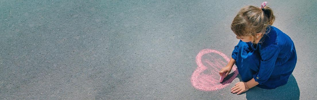 child draws with chalk on the pavement. Selective focus.