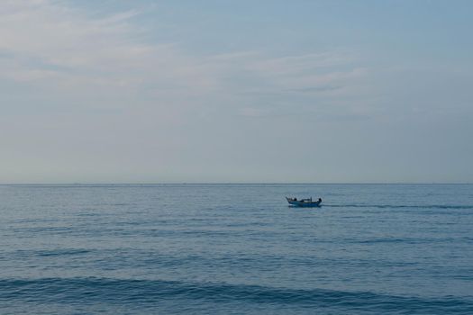 Simple background Calm dark blue sea fishing boat alone white pale Spindrift clouds Open way no limitations.