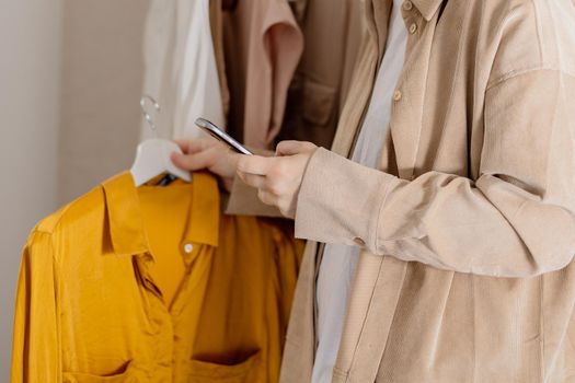 Woman holding smartphone and taking photo of her old clothes to sell them online. Selling on website, e-commerce. Reuse, second-hand concept. Conscious consumer, sustainable lifestyle. Close-up view