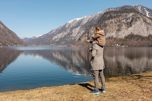 Father and son enjoying mountains, snow, lake, good weather, blue sky, sun. Little boy and his father spending time together. Family time. Beautiful landscape. Tourism, holiday, travel. Amazing view