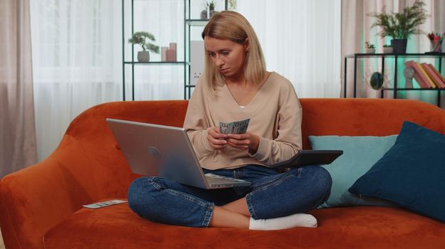 Planning family budget. Young woman counting money cash, calculate domestic bills working on laptop at home. Girl satisfied of income and saves money for a planned vacation, gifts, future expenses