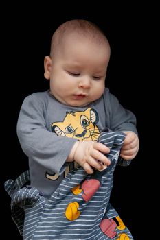 adorable baby trying to get dressed, black background. High quality photo