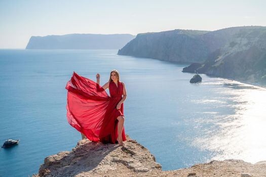 A woman in a red flying dress fluttering in the wind, against the backdrop of the sea