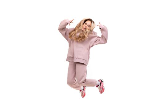 beautiful charismatic blonde in a pink tracksuit jumps on a white background, photo in a jump movement.