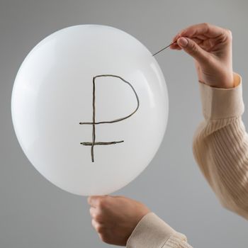 Caucasian woman pops a balloon with a ruble inscription with a needle