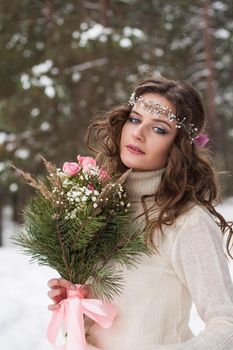 Beautiful bride in a white dress with a bouquet in a snow-covered winter forest. Portrait of the bride in nature.