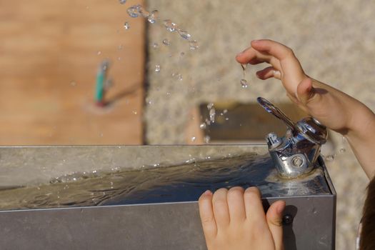 close-up of a child's hands playing with the water jet of a fountain