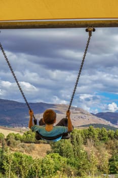 child with unrecognizable back swinging with a cloudy landscape in the background