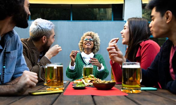 Multiracial friends enjoy some beer and laughing together in outdoors bar. Friendship and happiness concept.