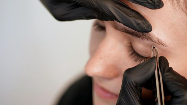 beauty saloon. close-up, hands of the cosmetician in black rubber gloves hold tweezers and pull out eyebrows. Master corrects the shape of the eyebrows. High quality photo