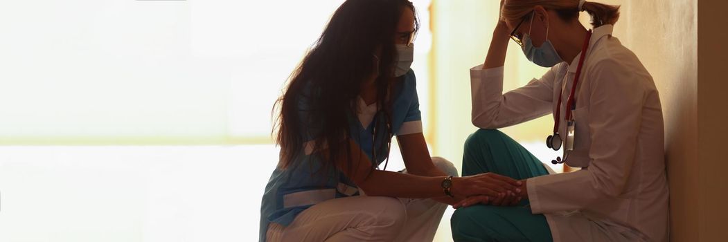 A female doctor calms down a tired colleague in the clinic, close-up. Stress of medical staff during a pandemic