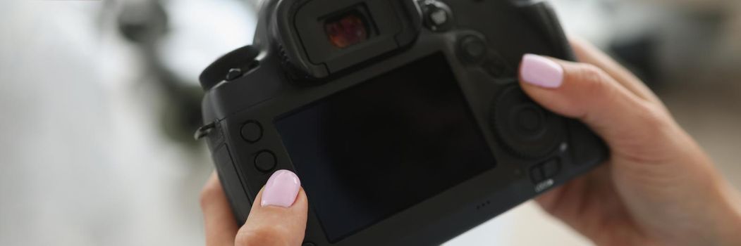 Female hands are holding a black digital camera, close-up, blurry. Photographer paparazzi pushing buttons on the device