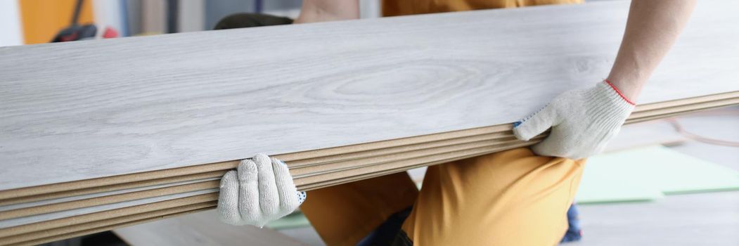 A man in uniform holds laminate panels, close-up. Repair in the apartment, replacing the floor covering in the room, laying parquet