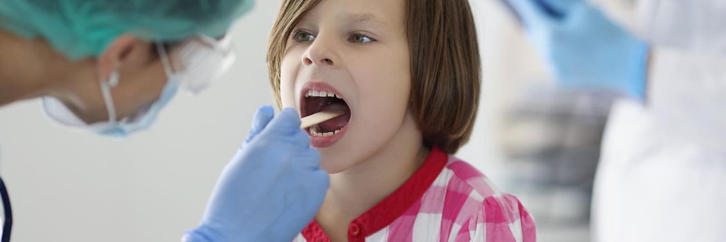 The doctor in the clinic looks at the throat of a little girl, close-up, blurry. Examination of a child by a pediatrician, diagnostics