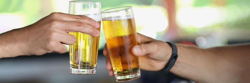 Male hands with glasses of beer clink glasses, close-up, blurry. Relax in a pub, party, craft beer tasting