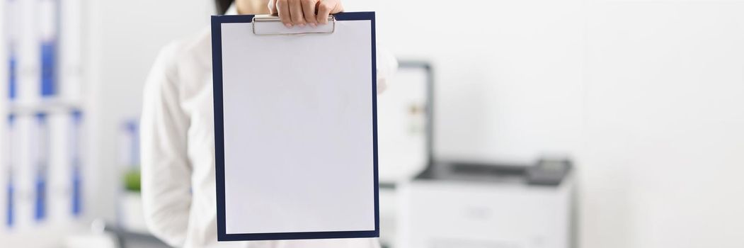 Woman in the office shows a folder with a blank document, mock up, close-up, blurry. Workspace, mentor businesswoman