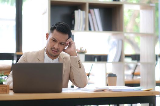 Tired frustrated young asian businessman feeling stressed holding head with hands, business problem failure concept.