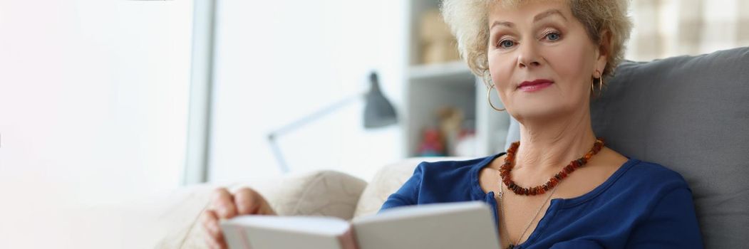 An elderly woman reads a book at home, close-up, blurry. Retirement age, leisure time during a pandemic