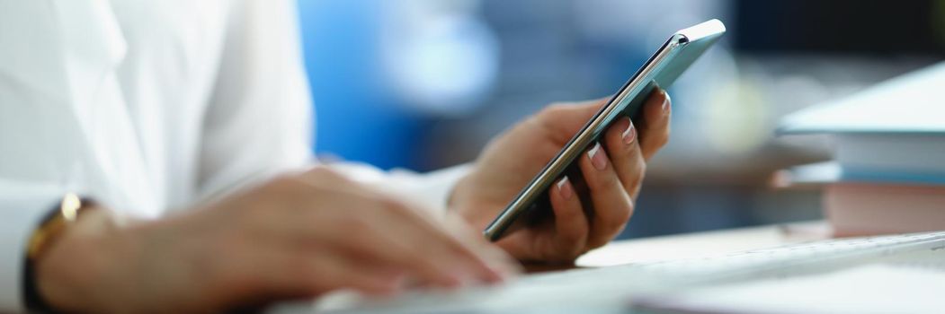 A woman works at a computer and holds a smartphone, close-up, blurry. Digital devices in the workplace, accounting department