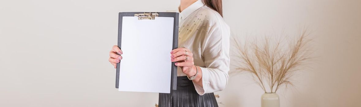 Woman holding clipboard with a blank sheet of paper. Blank paper poster in female hands.
