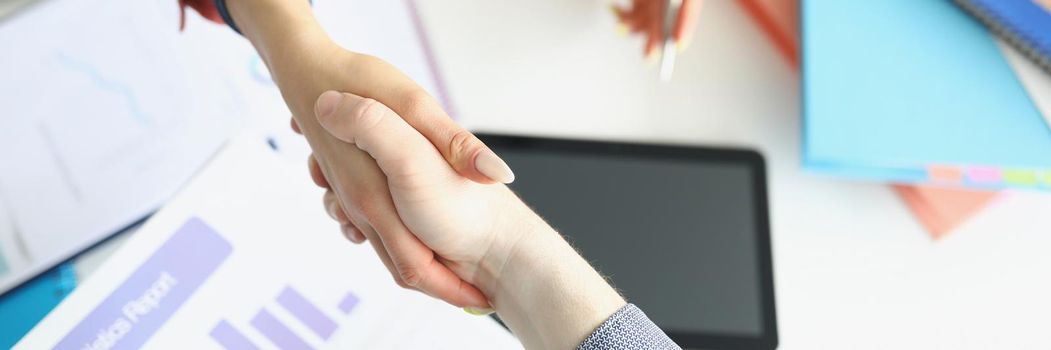 A woman in the office shakes hands with a man, there is a statistical report on the table, close-up, blurry. Approval of the report