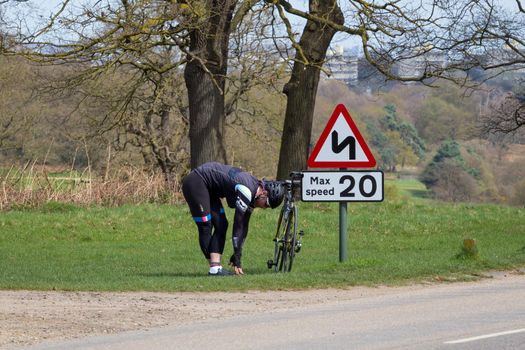 London, England - April 17 2018: Male cyclist stretching next to a speed sign in Richmond Park, London