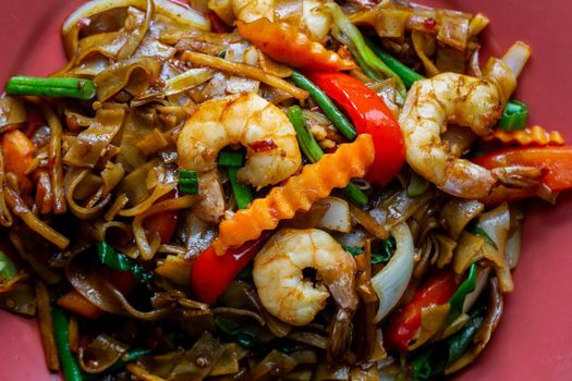 Drunken noodles, pad kee mao, with prawns, basil, chilii, peppers and green beans. Close-up on a plate.