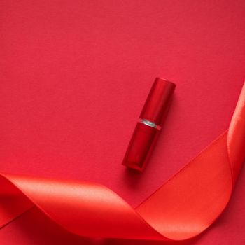 Cosmetic branding, glamour lip gloss and shopping sale concept - Luxury lipstick and silk ribbon on red holiday background, make-up and cosmetics flatlay for beauty brand product design