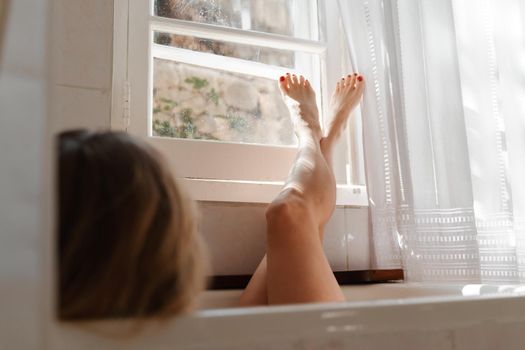 a beautiful mature woman massages her legs in a bath with candles in a cozy and comfortable atmosphere.