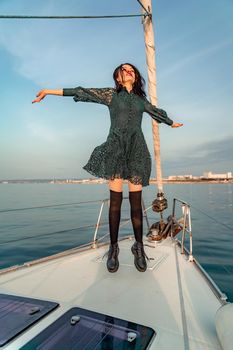 Woman standing on the nose of the yacht at a sunny summer day, breeze developing hair, beautiful sea on background.