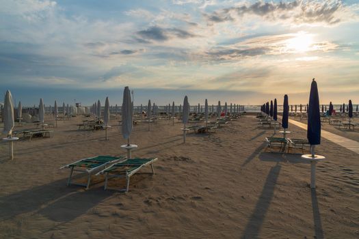 Sandy beach and close umbrellas beach at sunrise,typical italian adriatic beach.Summer vacation concept.Lido Adriano , Emilia Romagna,Italy.