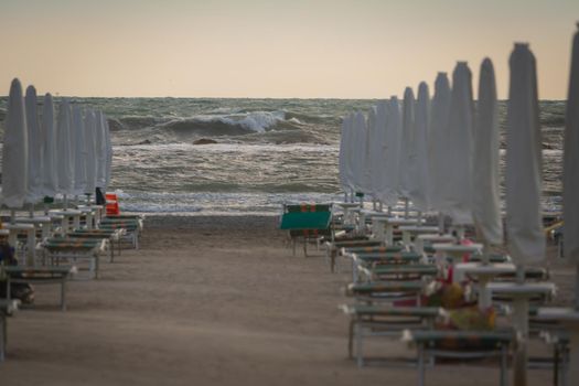 Big waves roll up on the beach. close parasol in bright Sunny day. White foaming waves and splashes.A hot summer day and high wave, seascape.Italy