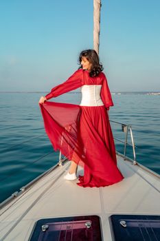 Attractive middle-aged woman in a red dress on a yacht on a summer day. Luxury summer adventure, outdoor activities