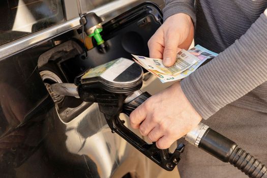 Car refuelling on petrol station. Man refilling car with fuel and holding money, euros. Close up. Gasoline, diesel is getting more expensive. Petrol industry and service. Petrol price and oil crisis